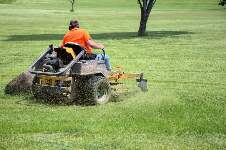 Senior retired male cutting the grass on expansive lawn using yellow zero-turn mower