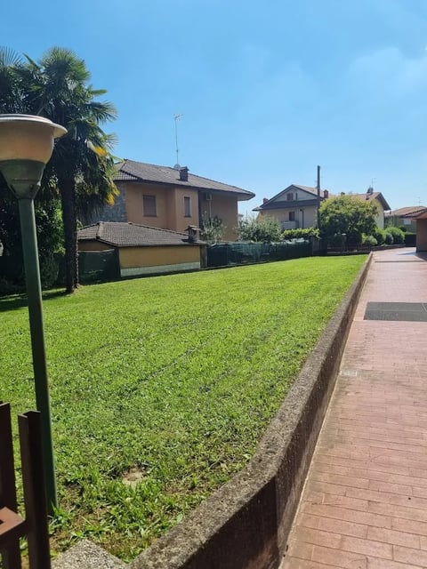 Residential street with large green lawn, brick pathway, and European-style houses under clear blue sky